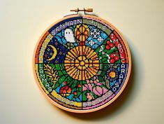 a colorful cross stitch pattern on a wooden hoop hanging from a wall mounted needle holder