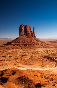 a large rock formation in the middle of desert land with dirt and rocks on both sides