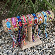 a small wooden bench covered in multicolored rope and tassels sitting on top of some rocks