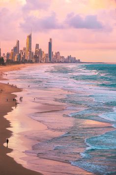 people are walking on the beach in front of some tall buildings and blue ocean water