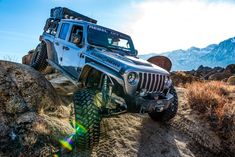 the jeep is driving through some rocks in the desert with mountains in the back ground