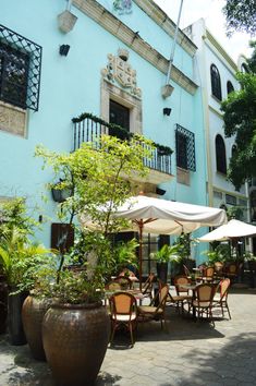 tables and chairs with umbrellas in front of a blue building on a sunny day