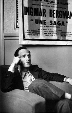 a black and white photo of a man sitting on a couch in front of a poster