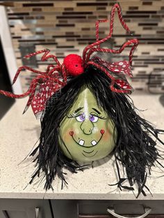 a green mask with black hair and red bow on it's head sitting on a counter