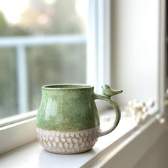 a green cup sitting on top of a window sill