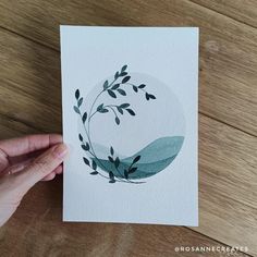 a hand is holding up a card with leaves on it and watercolor paper in the background