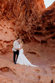 a bride and groom standing in the middle of a canyon with red rock formations behind them