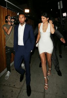 a woman in a white dress and a man in a suit walking down the street