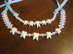 two necklaces made out of plastic teeth and pearls on a wooden table with blue ribbon