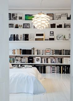 a room filled with lots of books on top of a white shelf next to a bed