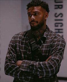 a man with his arms crossed wearing a black and white checkered shirt is looking at the camera