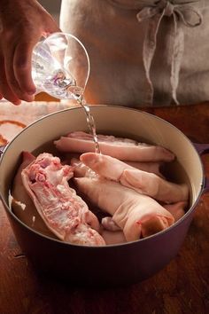 a person pouring water into a pot filled with meat