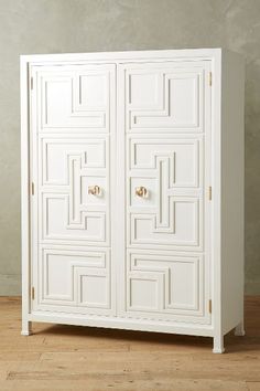 a white armoire sitting on top of a hard wood floor next to a wall