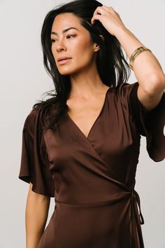 a woman in a brown dress is holding her hair