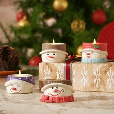 three snowman candles sitting on top of a table next to a christmas tree and presents