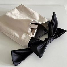 a black bow tie laying on top of a white bag next to a cell phone