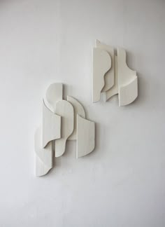 two white sculptures on the wall in an art gallery, one is shaped to look like abstract shapes