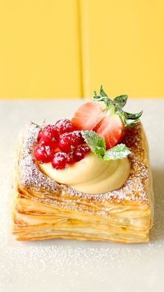 a pastry topped with berries and powdered sugar on top of a white table next to a yellow wall