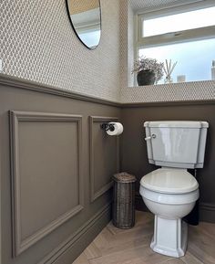 a white toilet sitting next to a window in a bathroom under a mirror on the wall