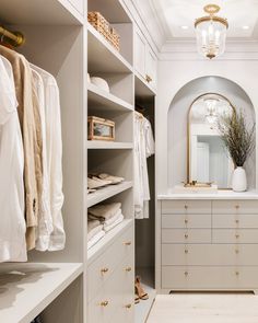 a walk - in closet with white cabinets and gold handles, an oval mirror on the wall