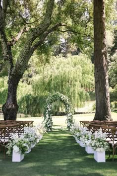 an outdoor ceremony setup with white flowers and greenery on the grass, surrounded by trees