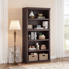 a book shelf with baskets and books on it in front of a window, next to a lamp