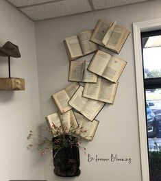 an arrangement of open books on the wall above a vase filled with flowers and plants