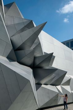 a woman is standing in front of a building that looks like an abstract structure with large, triangular shapes