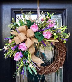 a wreath with pink flowers and green leaves hanging on the front door to welcome guests