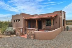 a small adobe style home sits in the desert with an outdoor patio and seating area