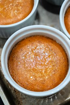 four baked desserts sitting in white cups on a metal tray, ready to be eaten