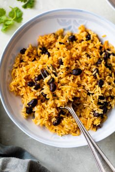 a white bowl filled with rice and beans next to a spoon on top of a table