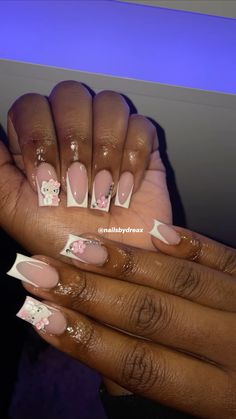 a woman's hands with pink and white nail polishes on her nails, holding a hello kitty manicure