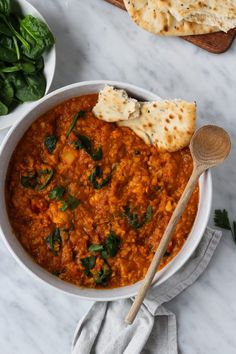 a white bowl filled with red lentula and spinach soup next to pita bread