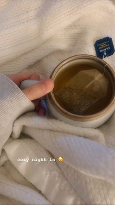 a person is holding their hand over a cup of tea on a white blanket with a blue tag that says cozy night in