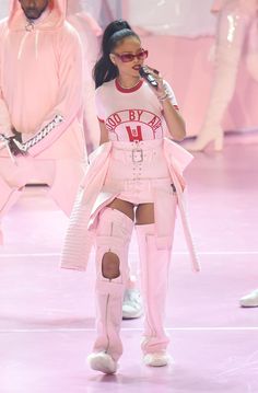 a woman in pink outfit and knee high boots walking on runway with other people behind her