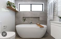 a white bath tub sitting next to a toilet under a window in a bathroom on top of a tiled floor