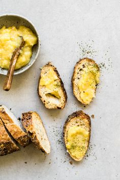 bread and butter on a table next to a bowl of dip sauce with two spoons