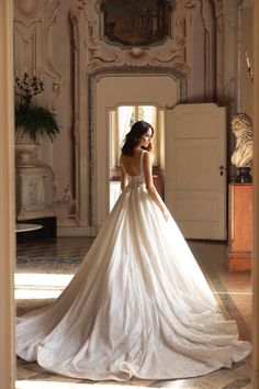 a woman in a white wedding dress is standing near a doorway and looking at the floor