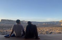 two people sitting on a ledge looking out at the desert