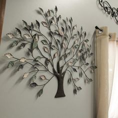 a metal tree is mounted on the wall next to a window with curtains and drapes