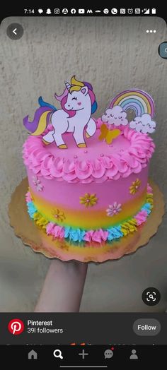 a hand holding up a cake decorated with pink frosting and rainbows on it