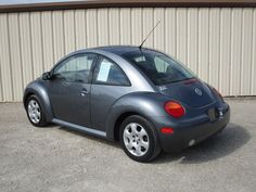 a small gray car parked in front of a metal building with no doors on it