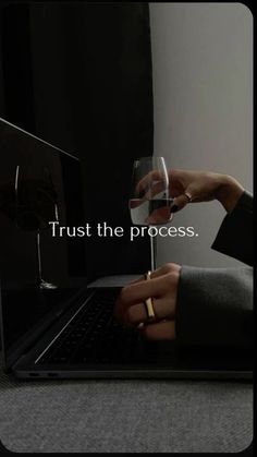 a person holding a wine glass in front of a laptop with the words trust the process