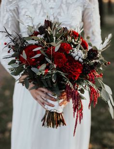 a woman holding a bouquet of red flowers and greenery