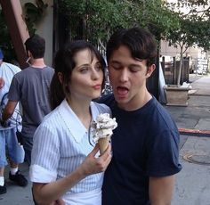 a man and woman standing next to each other eating an ice cream cone on the street