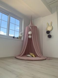 a pink canopy bed in the corner of a room with white walls and wooden floors