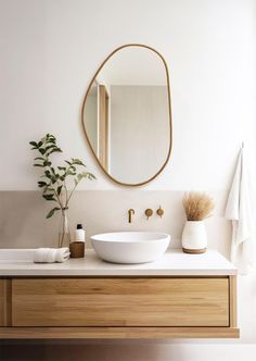 a white sink sitting under a mirror next to a wooden cabinet and vase with plants