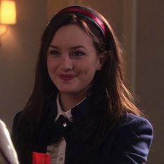 a woman with long hair wearing a blue jacket and red headband smiles at the camera