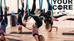 a group of women doing aerial acrobatics on yoga mats in a gym